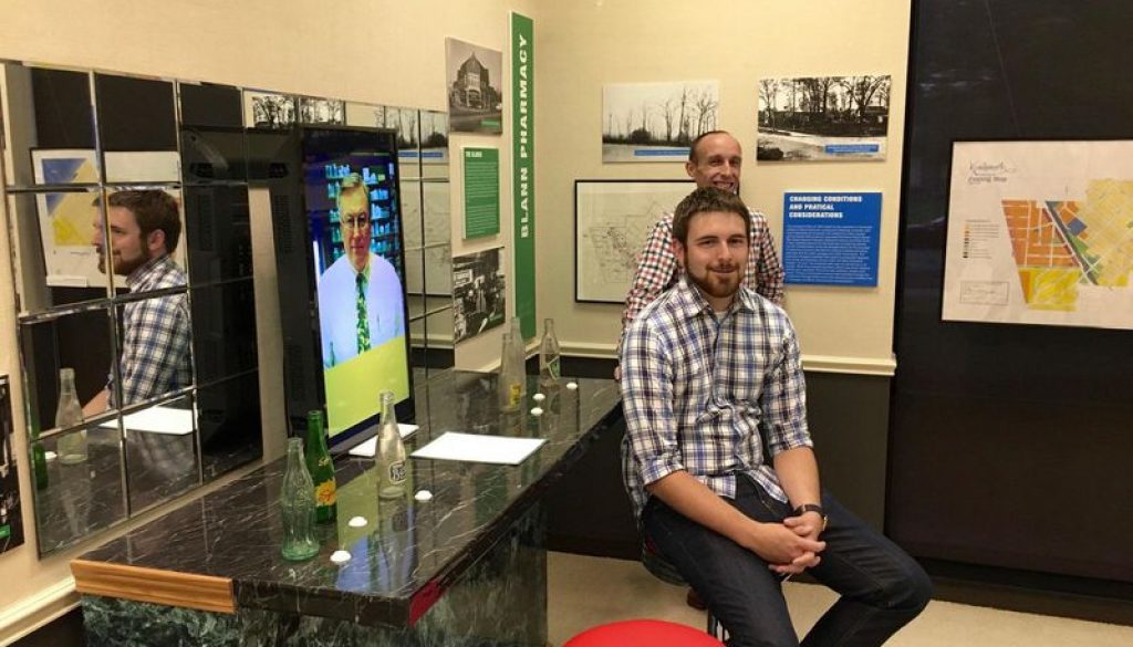 Jeremy Murray, rear, and Kyle Mathers, respectively the Kenilworth Historical Society’s collections manager and curator, sit at the Blann Pharmacy soda fountain mockup central to “How Can I Help You: Business and Commerce in Kenilworth.” The mockup allows visitors to hear an oral history of the pharmacy, from Robert Stensby, its last owner. The exhibition runs through October.(Kathy Routliffe/Pioneer Press)